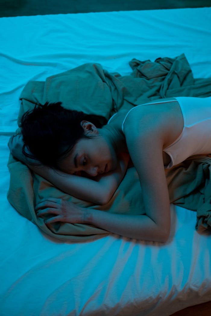 services-01 An adult woman lies on a bed in a dimly lit room, reflecting emotions of solitude and contemplation.